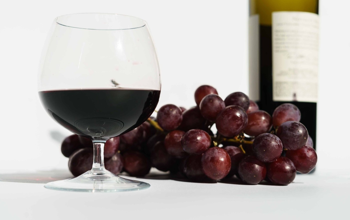 Rødvinsglas med druer og en flaske vin